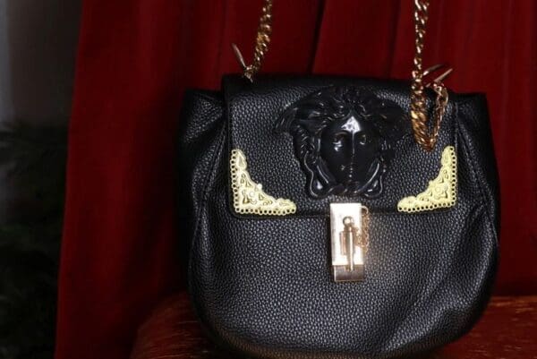 A black purse with gold chain and a metal lock.