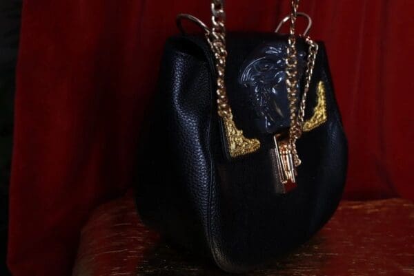 A black purse with gold chain and lock on top of a table.