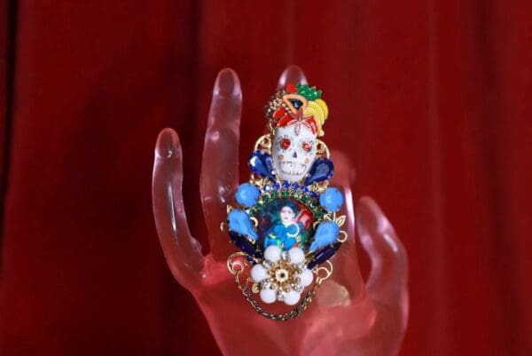 A hand holding a colorful skull ring with flowers.
