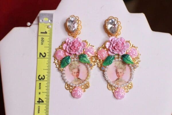 A pair of earrings with pink roses and a picture.