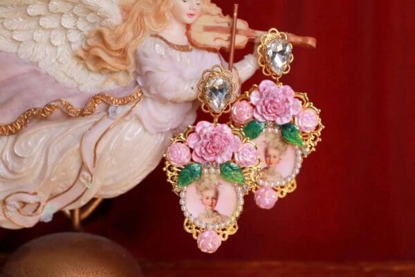 A pair of pink earrings with flowers and green leaves.