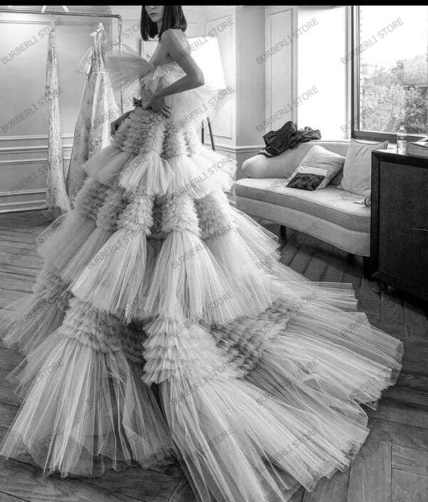 A woman in a long dress standing next to a couch.