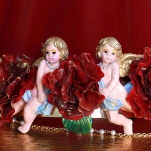 Two angels sitting on top of a table with red flowers.
