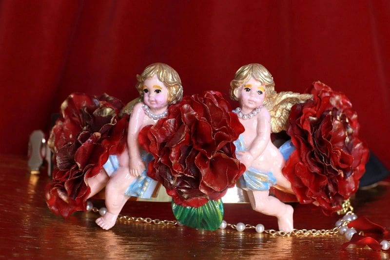 Two angels sitting on top of a table with red flowers.