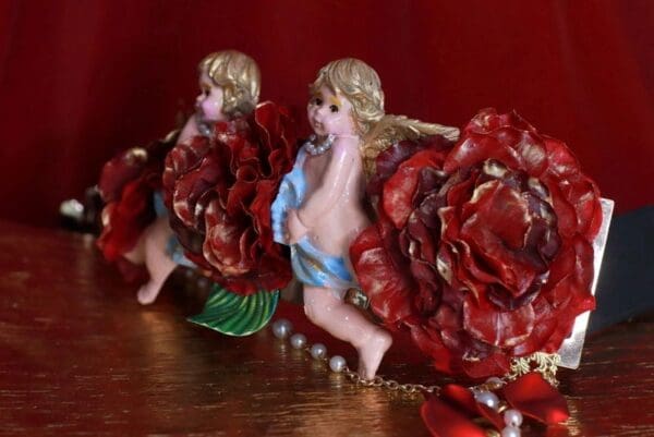 Two angels are sitting on a table with red roses.