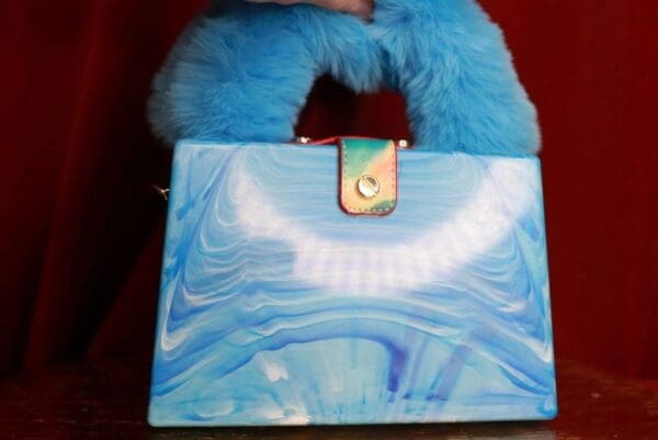 A blue purse with a furry handle and some clouds