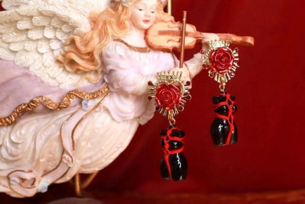 A red and black earrings hanging from the side of a gold angel.