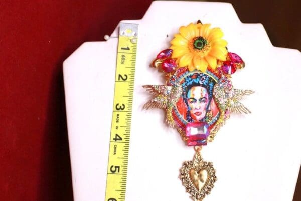 A large brooch with a picture of frida kahlo and a yellow flower.