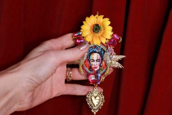 A hand holding a necklace with a flower on it.
