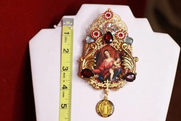 A large gold plated religious medal with a virgin mary and jesus.