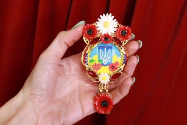 A person holding up a ukrainian pendant with flowers.