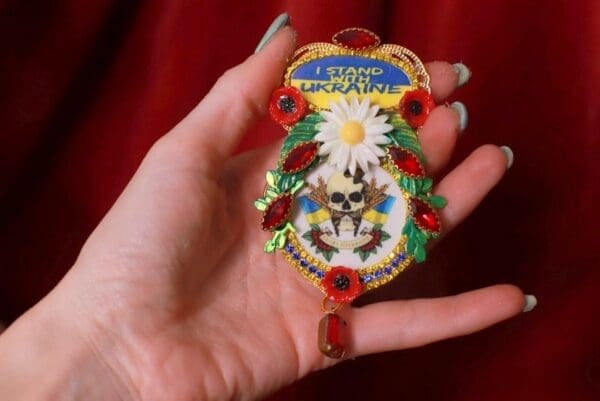 A hand holding a colorful ornament with flowers and skulls.