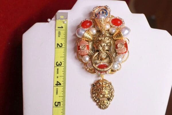 A gold and red pendant with a ruler next to it
