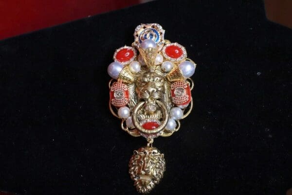 A gold and red brooch with pearls on top of it.