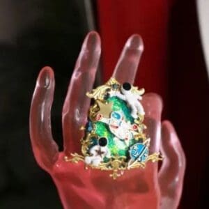 A hand holding something with gold and green beads.