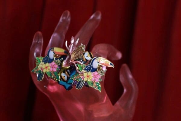 A hand holding two colorful rings with flowers and birds.