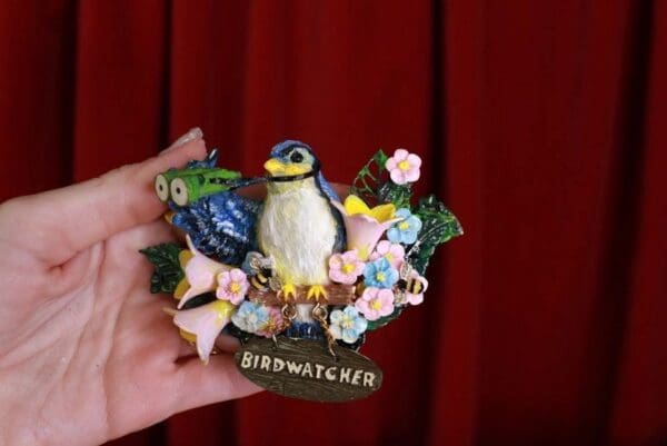 A hand holding a bird watcher pin.