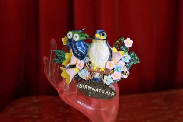 A bird figurine sitting on top of a pink hand.