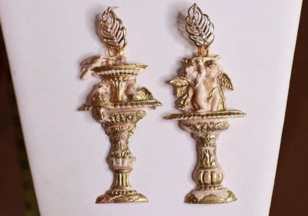 A pair of gold candles with angel and leaf designs.