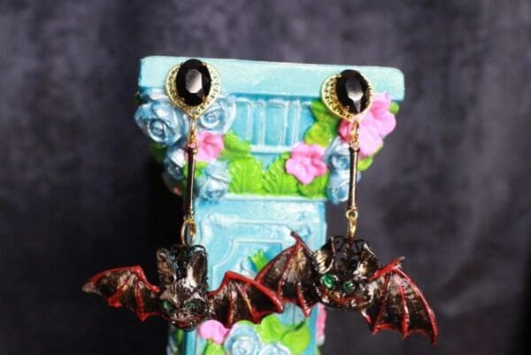 A pair of earrings with bats hanging from them.
