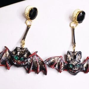 A pair of bat earrings hanging on top of a white board.