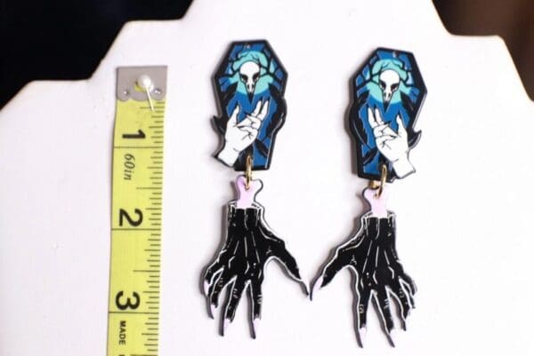 A pair of earrings with a skeleton hand and coffin.