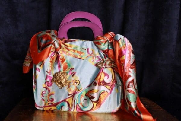 A colorful purse with a pink handle and a scarf around the top.