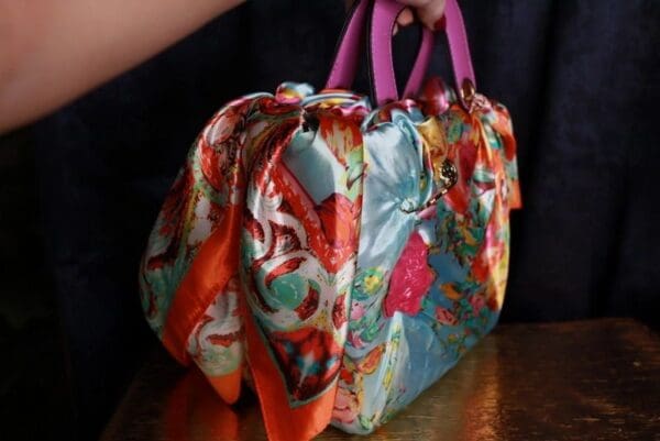 A woman holding onto the handle of a colorful bag.