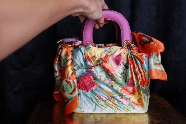 A woman holding onto the handle of a colorful purse.