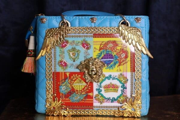 A blue purse with gold chains and a lion head.