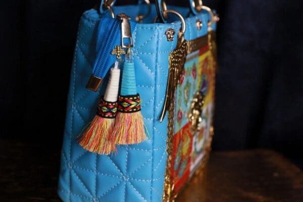 A blue purse with tassels and charms on the handle.