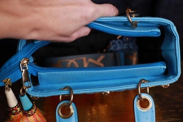 A person holding onto the handle of a blue purse.