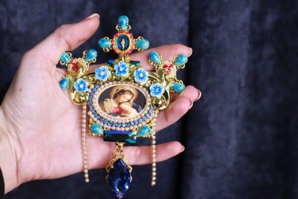 A person holding onto a small blue and gold pendant