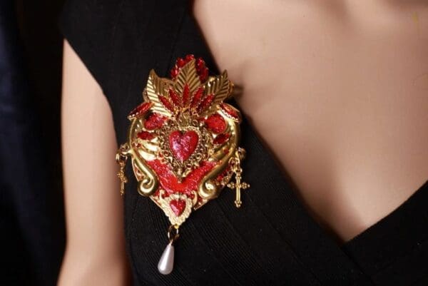 A woman wearing a red and gold heart shaped brooch.