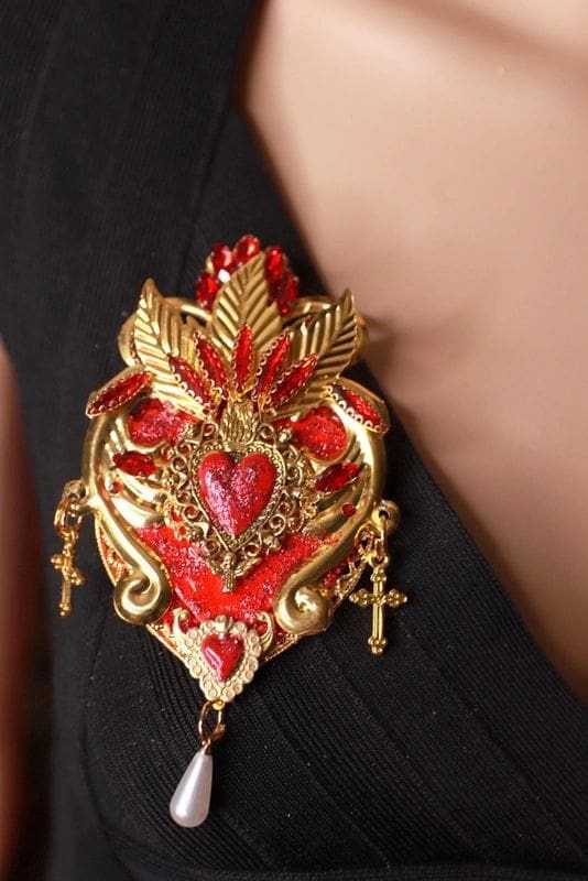 A woman wearing a red and gold heart shaped brooch.