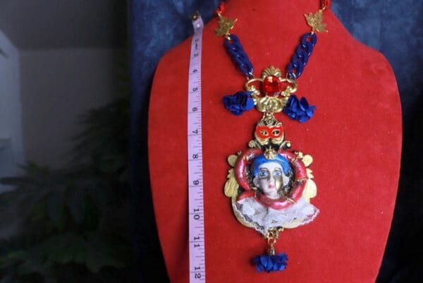 A red mannequin wearing a necklace with blue beads and a face.