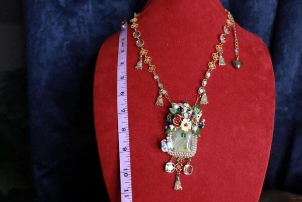 A red mannequin wearing a necklace with flowers and dangling beads.