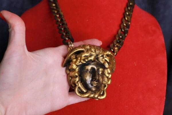 A person holding onto a chain with a gold medusa head.