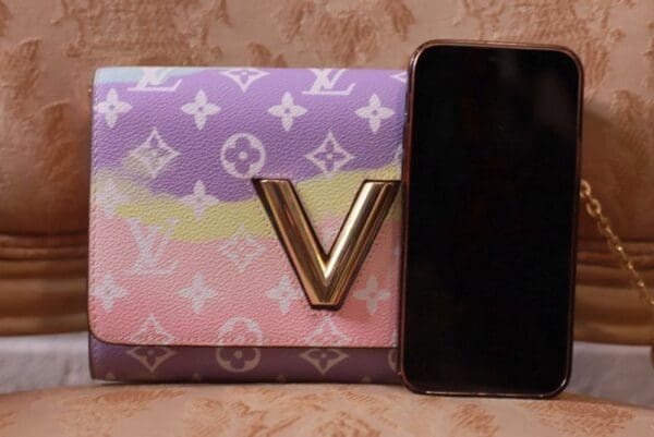A phone sitting next to a louis vuitton wallet.