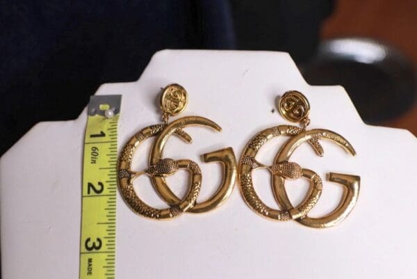 A pair of gold earrings on display next to a ruler.