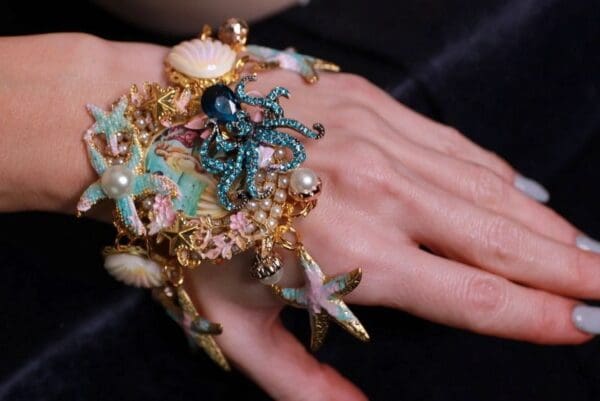 A woman 's hand wearing a bracelet with sea creatures on it.