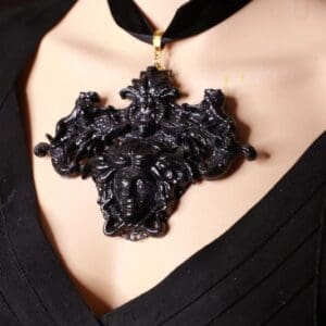 A woman wearing a black necklace with a cross shaped pendant.