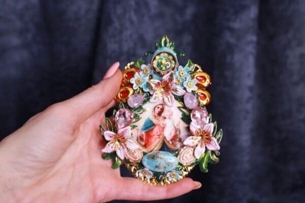 A hand holding a small round ornament with flowers.