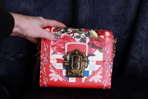 A person holding onto the side of a red purse.