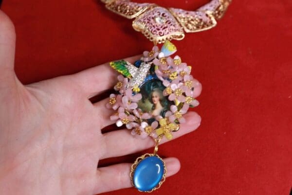 A hand holding onto a necklace with a blue stone