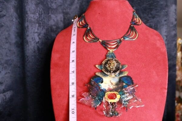 A red mannequin wearing a necklace with an image of a man in the middle.