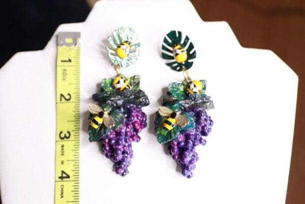 A pair of earrings with grapes and bees on them.