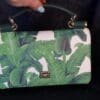 A woman holding onto a green purse with banana leaves on it.