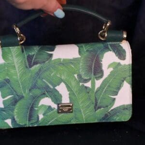A woman holding onto a green purse with banana leaves on it.