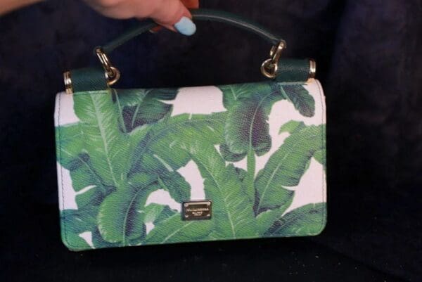 A woman holding onto a green purse with banana leaves on it.